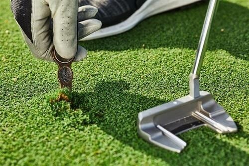 Golfhanske reparerer et nedslagsmerke på greenen med reparasjonsverktøy