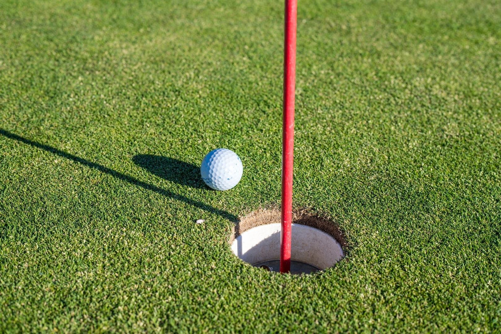 Golfball ved et hull med rødt flagg på en tettklipt green
